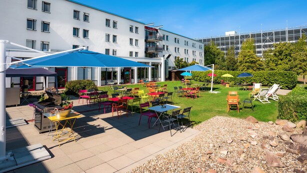 Un espace extérieur aménagé en terrasse, avec plusieurs tables et chaises, un barbecue et des parasols pour créer de l’ombre.