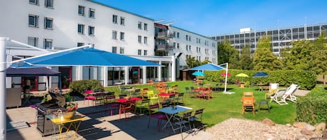 Un patio al aire libre con varias mesas y sillas, una parrilla y sombrillas que dan sombra.