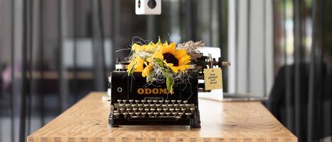 Une machine à écrire ancienne, ornée d’un motif de tournesol, posée sur une table en bois dans un décor moderne.