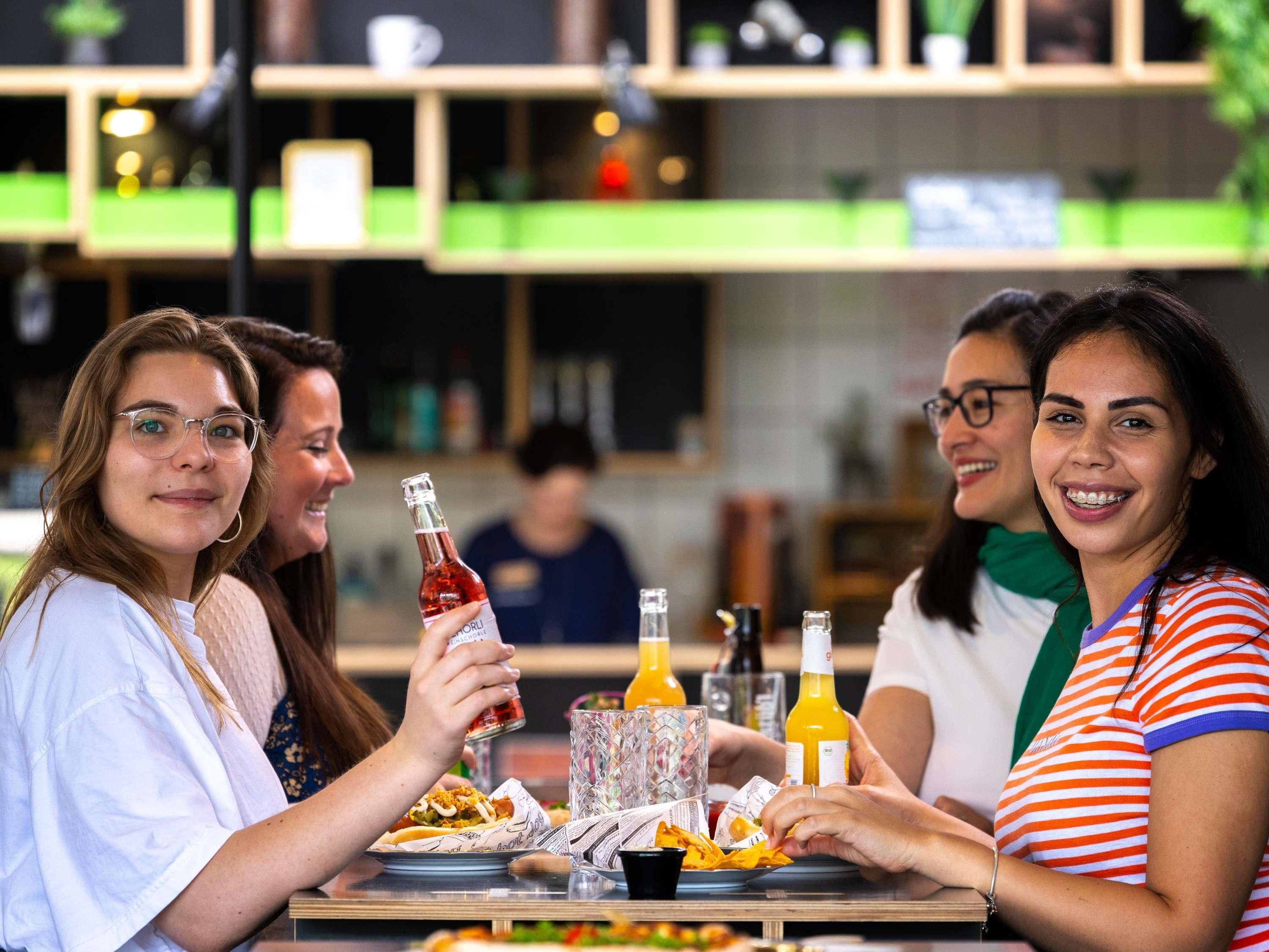 Un grupo de personas cenando en un restaurante con una decoración moderna, que incluye una barra y estanterías con objetos.