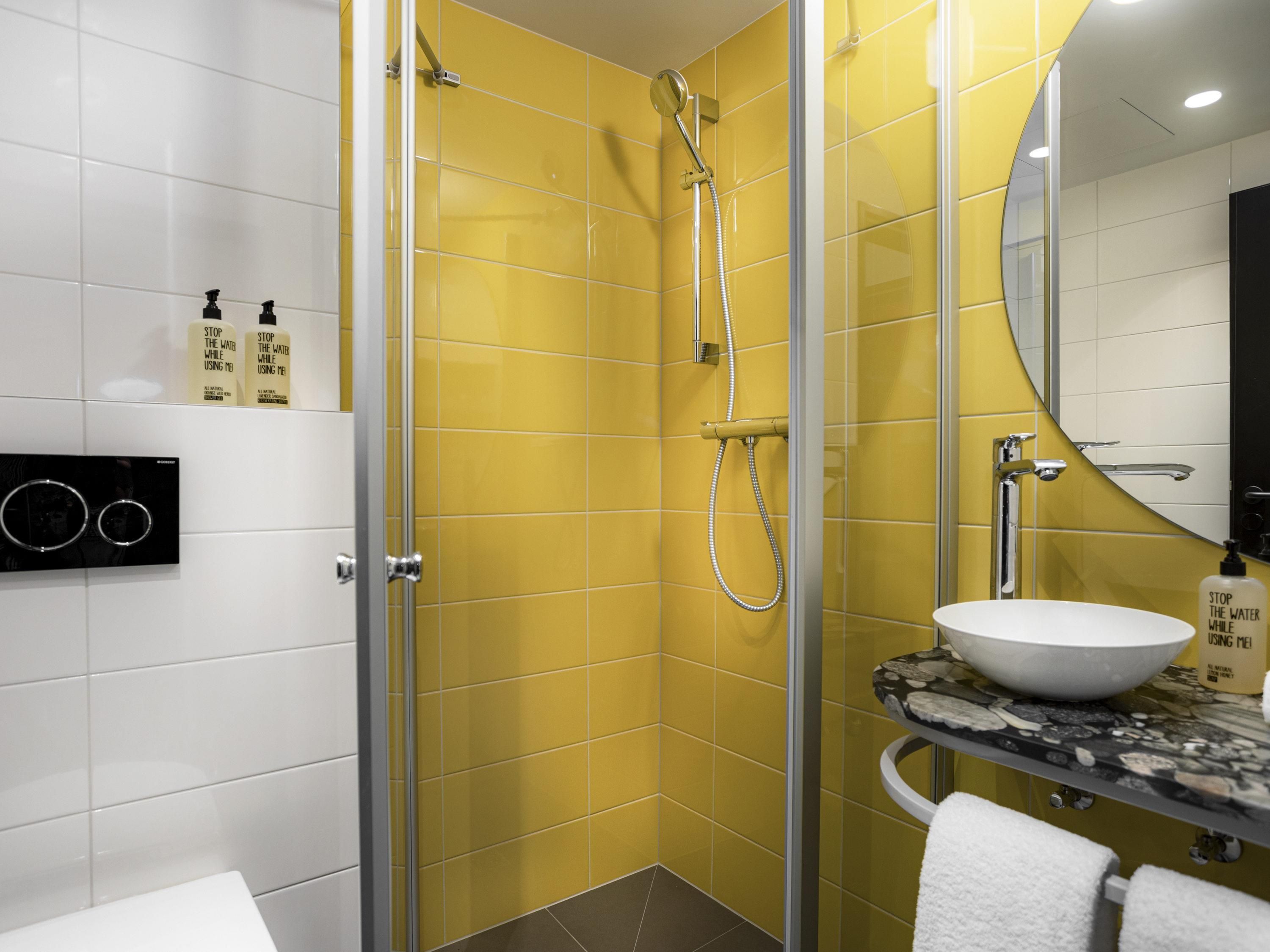 A modern bathroom with yellow tiles, a glass-enclosed shower, a white sink, and a mirror.