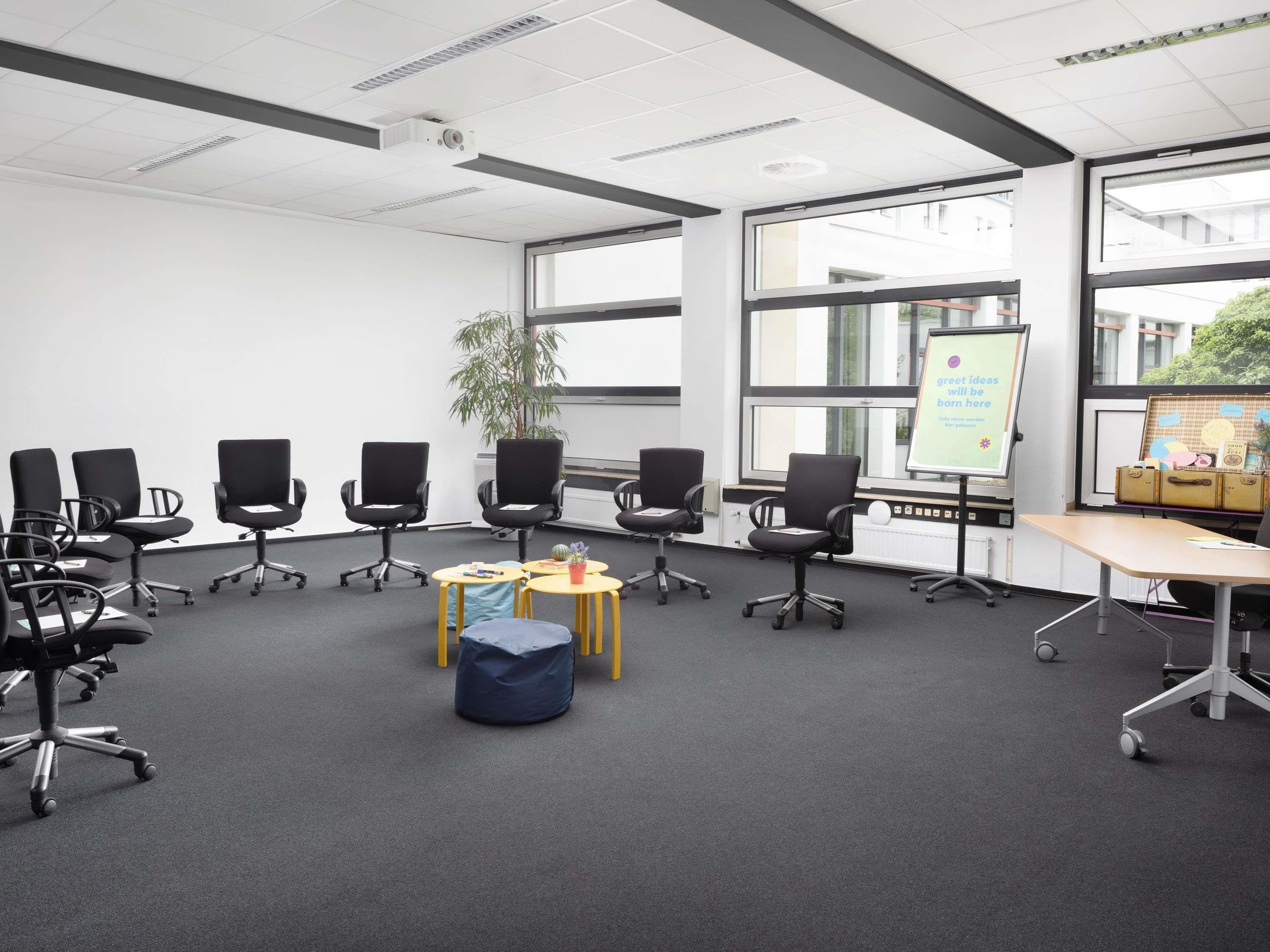 Een vergaderruimte met zwarte bureaustoelen, een whiteboard en een plant.