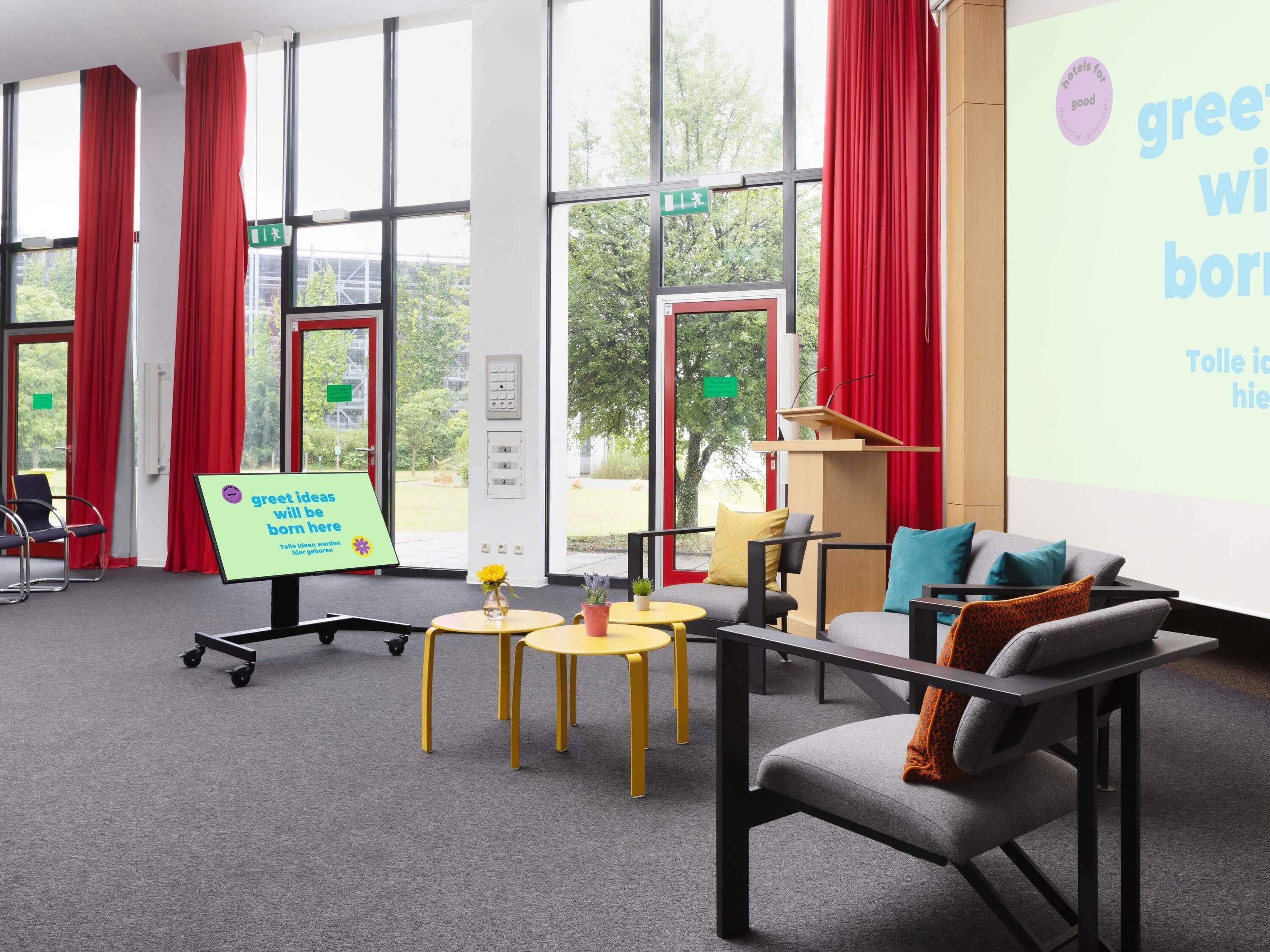 A modern hotel room with large windows, red curtains, a projector screen, and a sign promoting green ideas.
