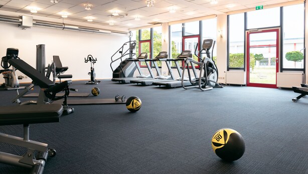 Een fitnessruimte met loopbanden, elliptische trainers en losse gewichten.
