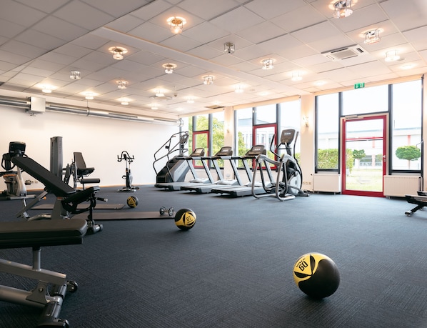 Een fitnessruimte met loopbanden, elliptische trainers en losse gewichten.