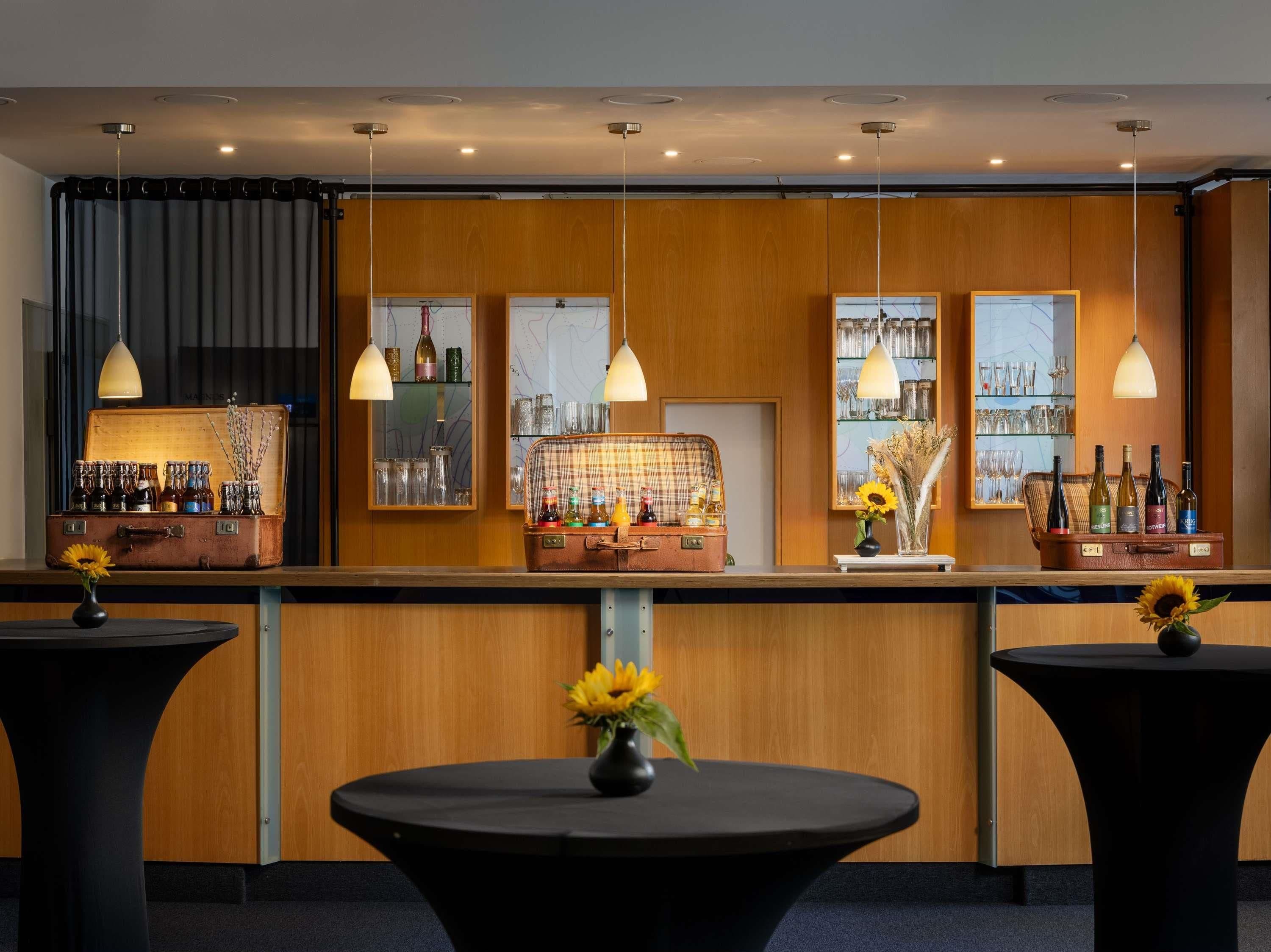 Una zona de bar con paneles de madera, iluminación colgante y una exhibición de maletas antiguas.