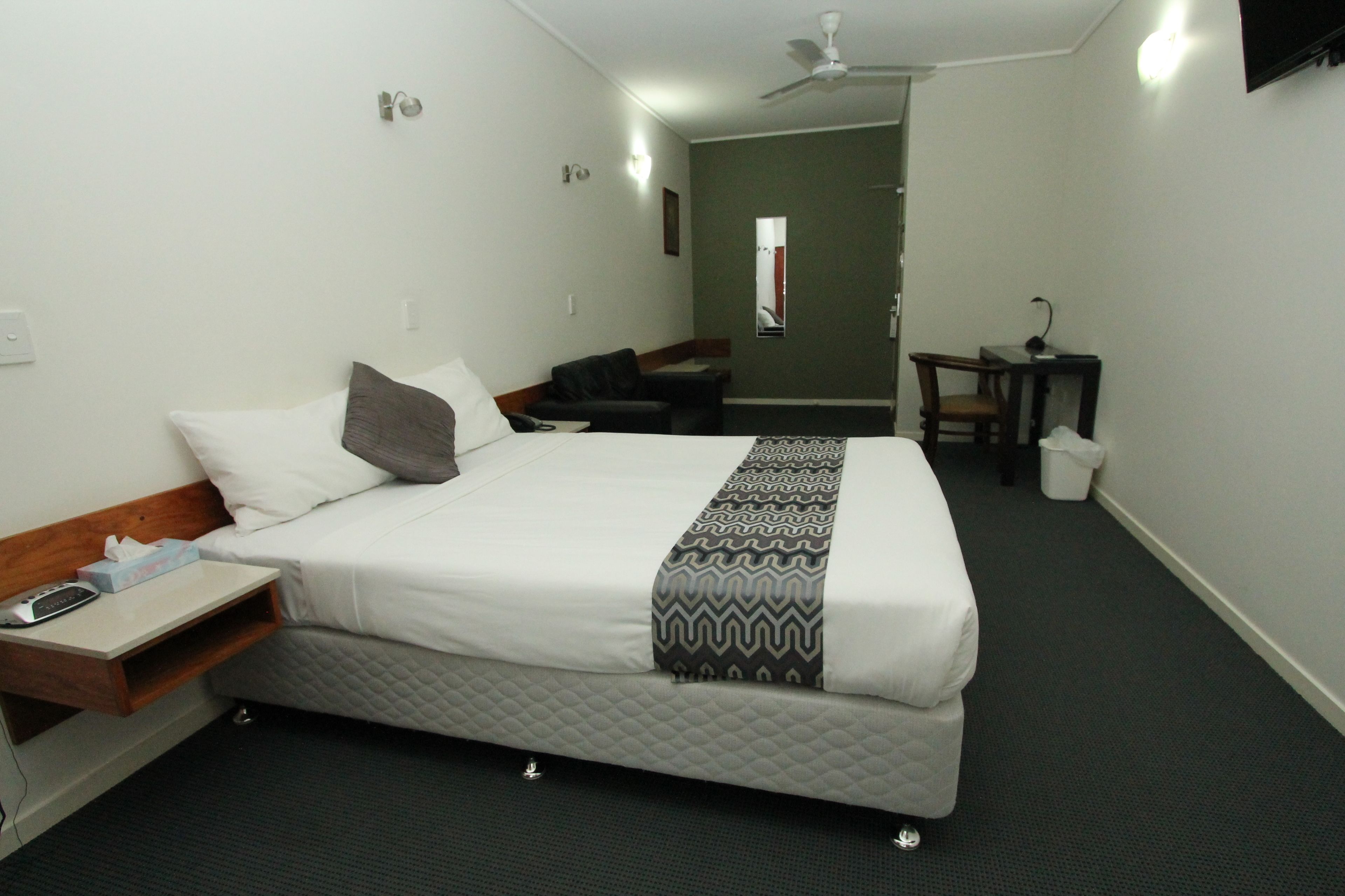 Een hotelkamer met een bed, nachtkastje en een klein bureau met stoel.