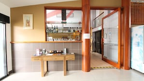 Un mostrador de recepción con una barra que exhibe diversos artículos, un pilar de madera y una pared con azulejos.