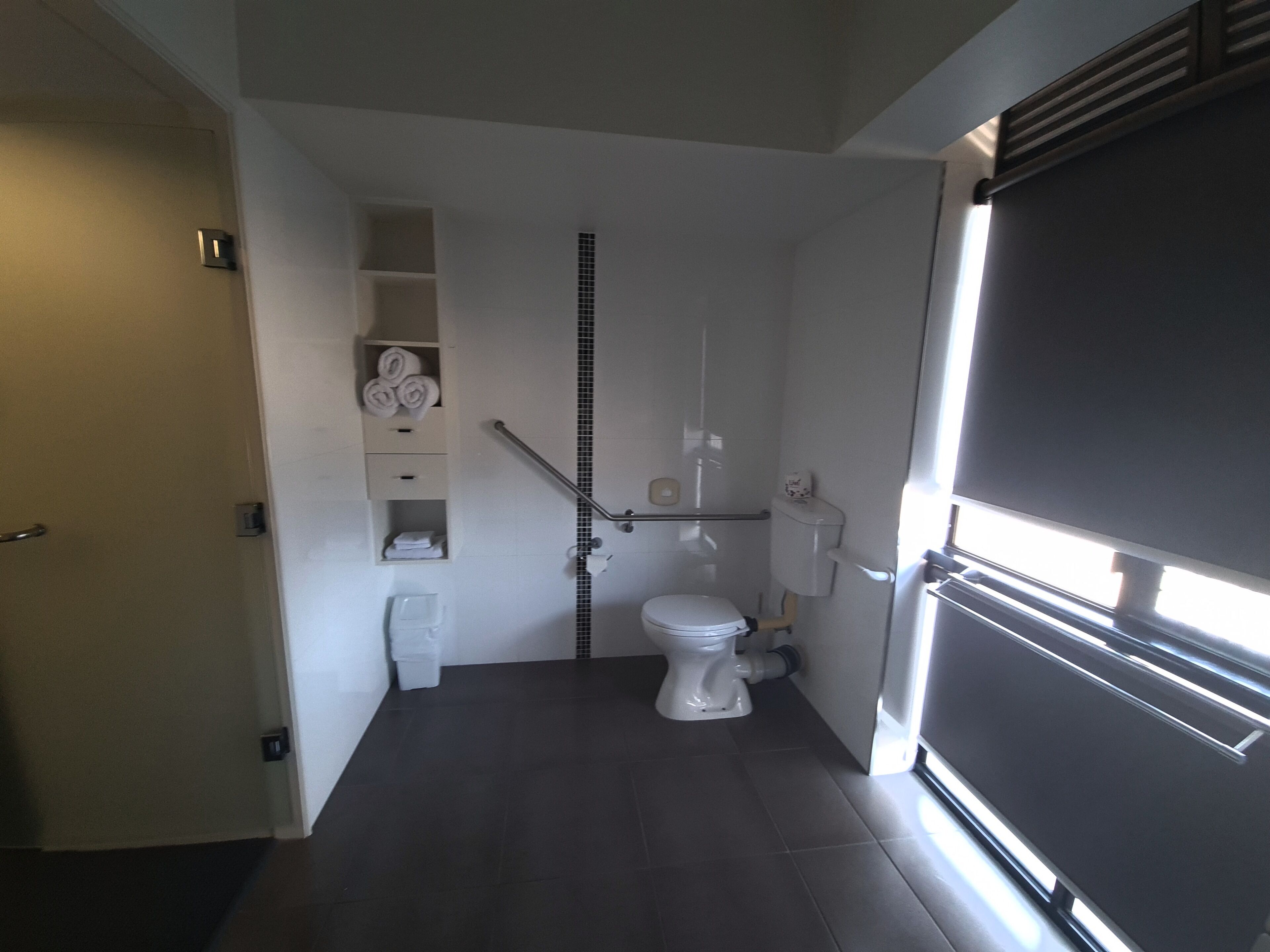 Een kleine badkamer met toilet, een handgreep en een plank met handdoeken.