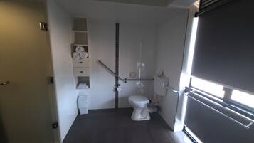 Een kleine badkamer met toilet, een handgreep en een plank met handdoeken.