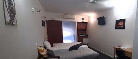 Una habitación de hotel compacta con cama, escritorio, silla, microondas y una pequeña kitchenette.