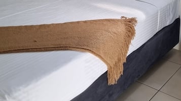 Ein Bett mit weißen und roten Kissen, einer braunen Tagesdecke und einem Fenster mit blauegardinen.