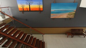 Una escalera con escalones de madera y barandillas de metal, que conduce a una plataforma con un banco y dos cuadros en la pared.