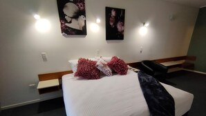 Una habitación de hotel con una cama grande, dos luces fijadas a la pared y dos cuadros con motivos florales.