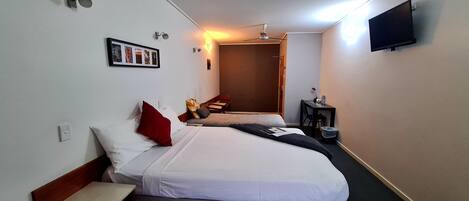 A hotel room with two beds, a flat-screen TV, a ceiling fan, and a small table with a lamp.