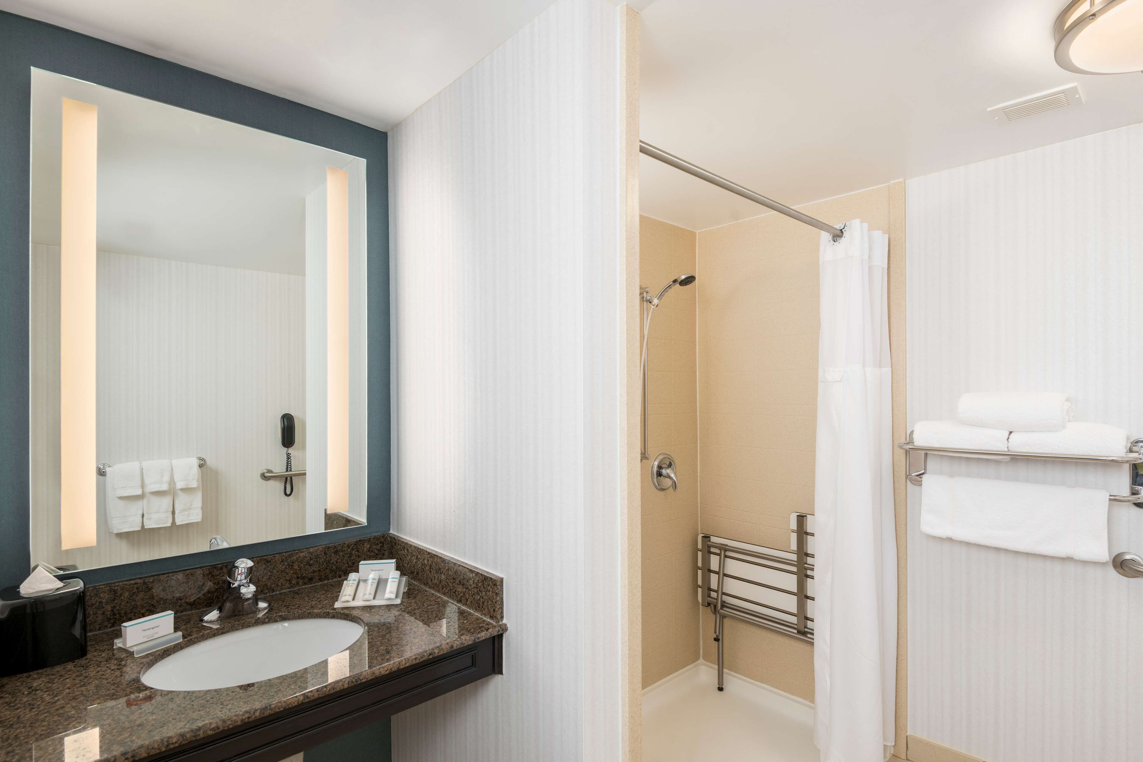 A modern bathroom with a granite countertop sink, a large mirror, a shower with a glass door, and a towel rack with folded towels.