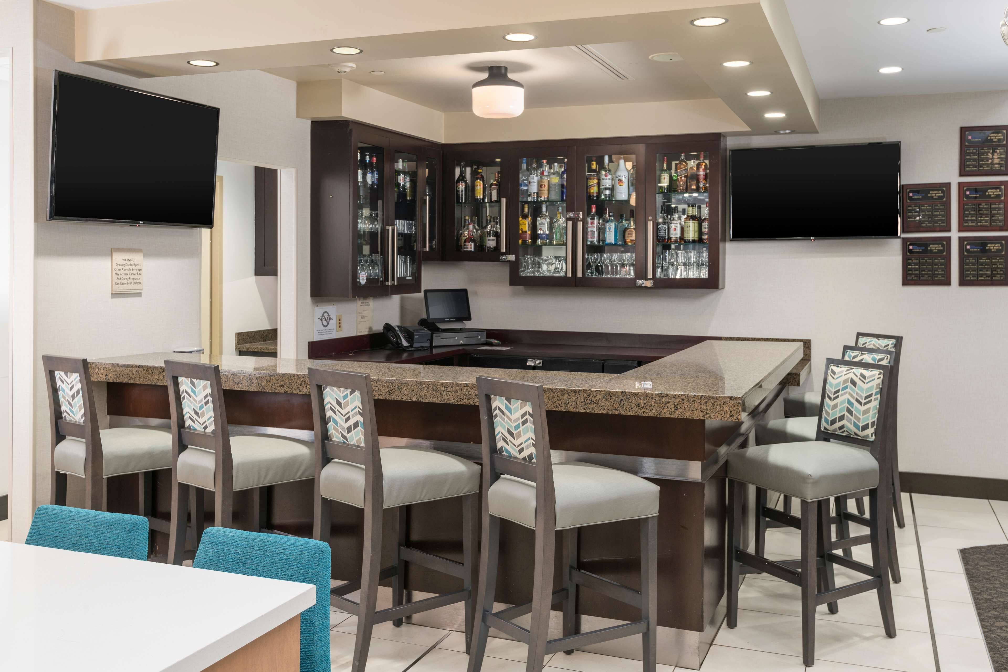 A bar area with a granite countertop, bar stools, and a television mounted above.