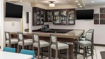 A bar area with a granite countertop, bar stools, and a television mounted above.