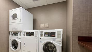 A laundry room with three stacked washing machines and two signs on the wall.