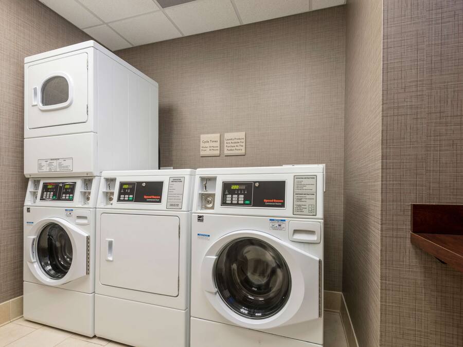 A laundry room with three stacked washing machines and two signs on the wall.