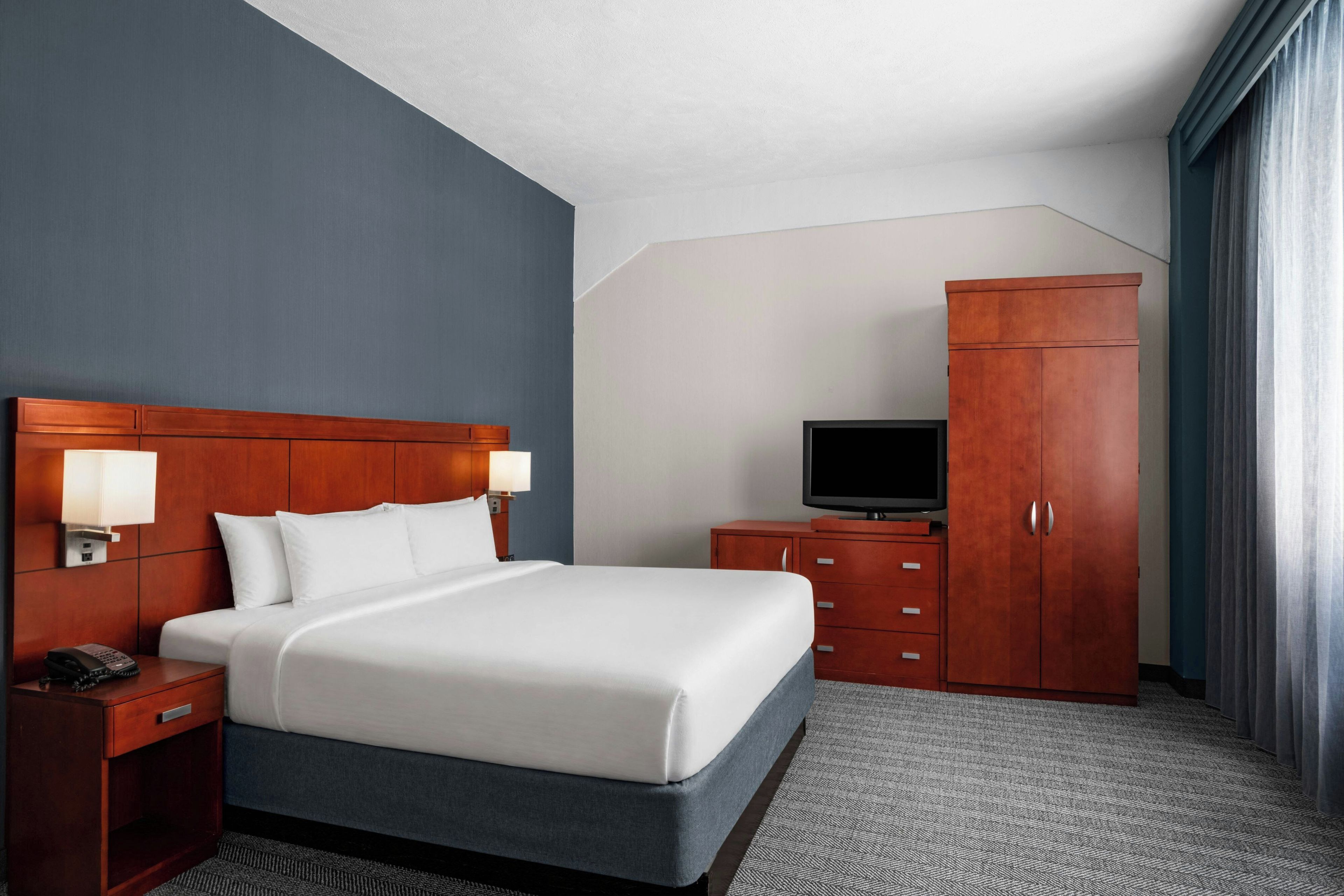 Una habitación de hotel con cama, televisión, armario y escritorio con teléfono.