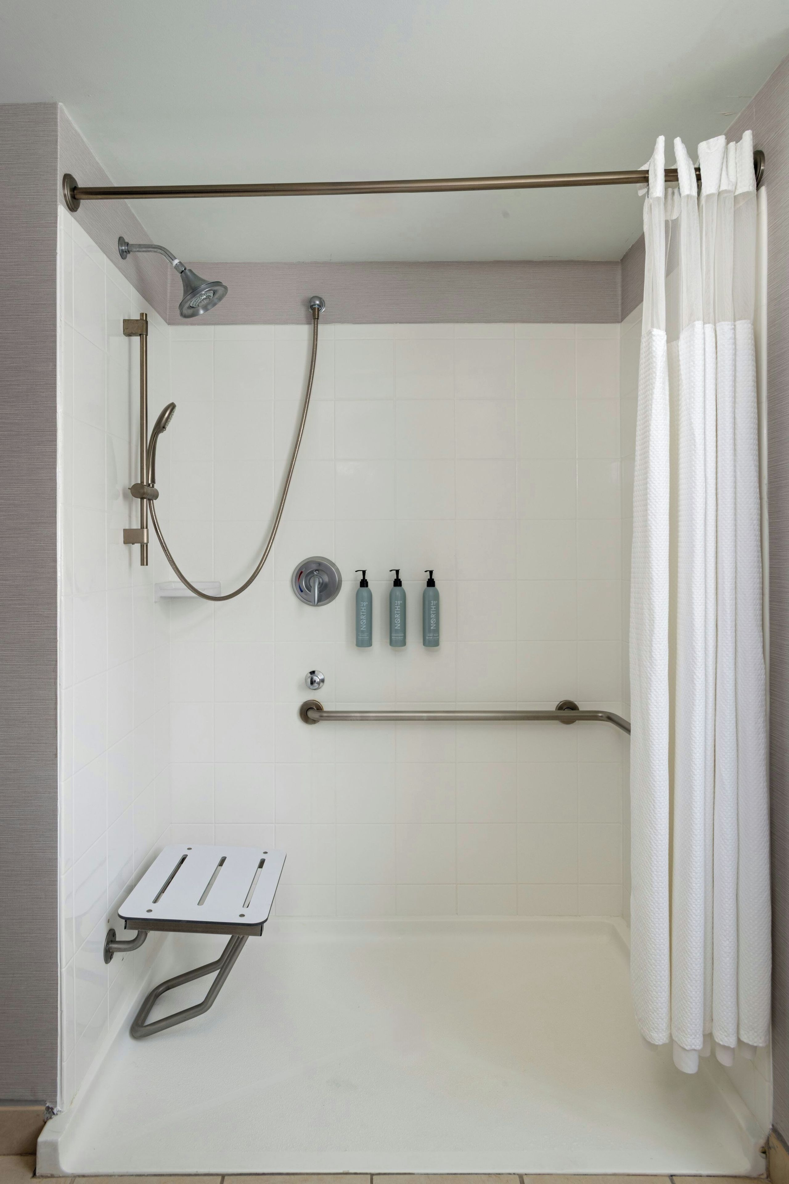 A modern shower area with a handheld showerhead, a handheld shower attachment, and a grab bar.