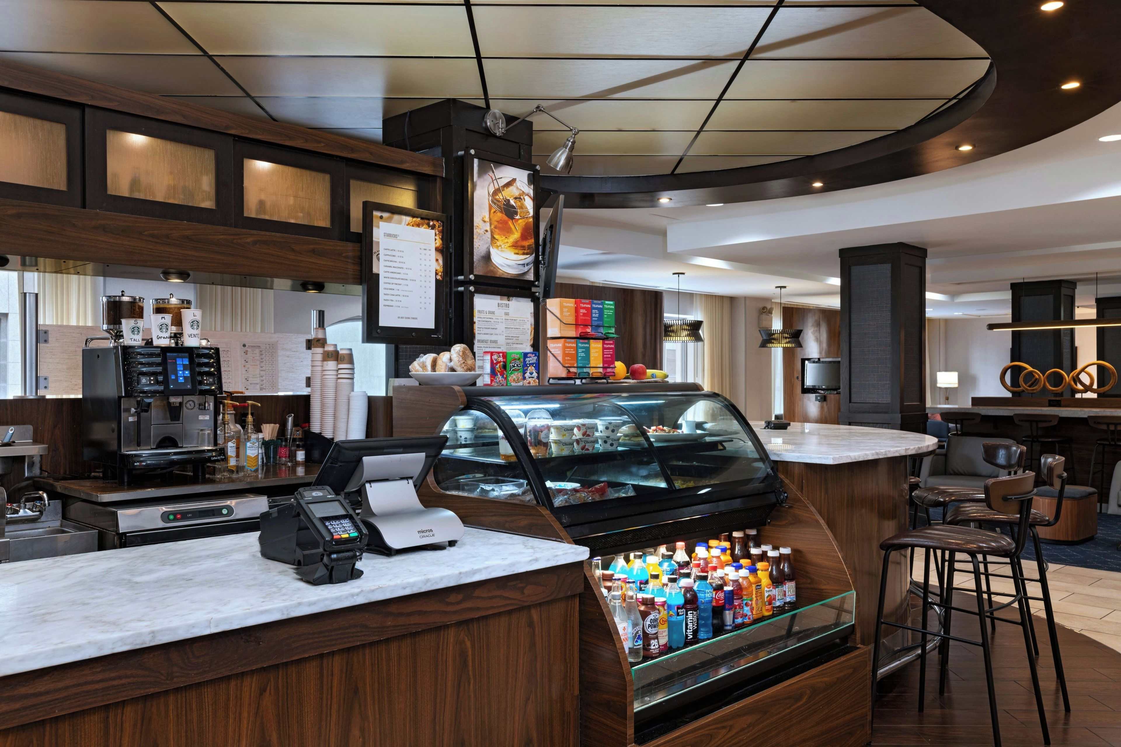 A modern coffee shop with a counter, espresso machines, a cash register, a menu board, and a refrigerated display case.