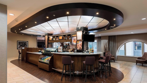 A modern bar area with a curved counter, bar stools, and a large screen. - Courtyard by Marriott Tulsa Downtown (Tulsa)