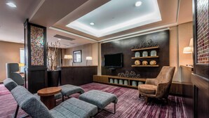 A modern lounge area with seating, a flat-screen TV, decorative shelves, and a patterned carpet. - Courtyard by Marriott Tulsa Downtown (Tulsa)