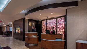 A hotel reception area with two wooden reception desks, a patterned wall, and a visible exit sign. - Courtyard by Marriott Tulsa Downtown (Tulsa)