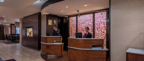 Et hotellets receptionsområde med to trædiske, en mønstret væg og et synligt skilt til udgang.