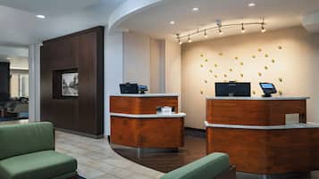 A hotel reception area with two reception desks, a framed picture on the wall, and a seating area with green upholstered chairs.
