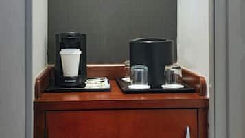 Un mini bar con cafetera, una jarra de vidrio y dos vasos sobre una bandeja de madera.