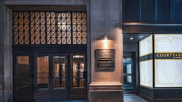 Entrada de un edificio con una puerta metálica, un letrero que dice 'Home of the Tulsa Press Club' y un letrero de 'Courtyard by Marriott'.