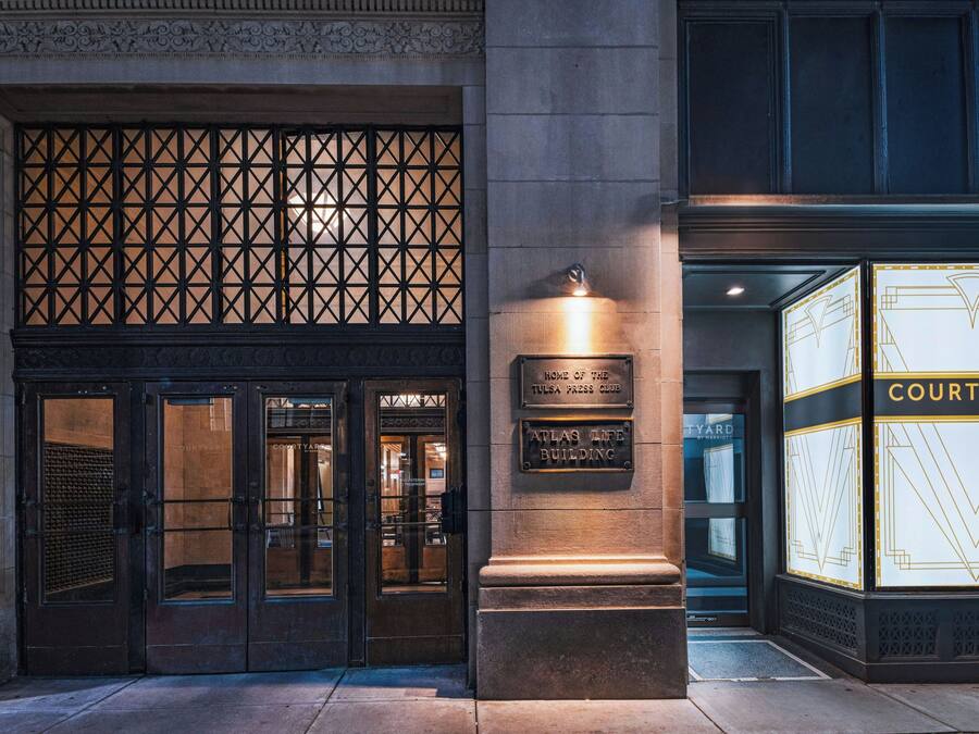 Entrada de un edificio con una puerta metálica, un letrero que dice 'Home of the Tulsa Press Club' y un letrero de 'Courtyard by Marriott'.