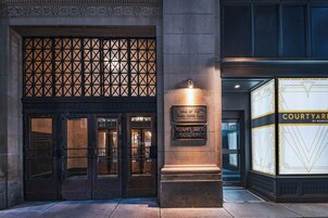 Entrada de un edificio con una puerta metálica, un letrero que dice 'Home of the Tulsa Press Club' y un letrero de 'Courtyard by Marriott'.