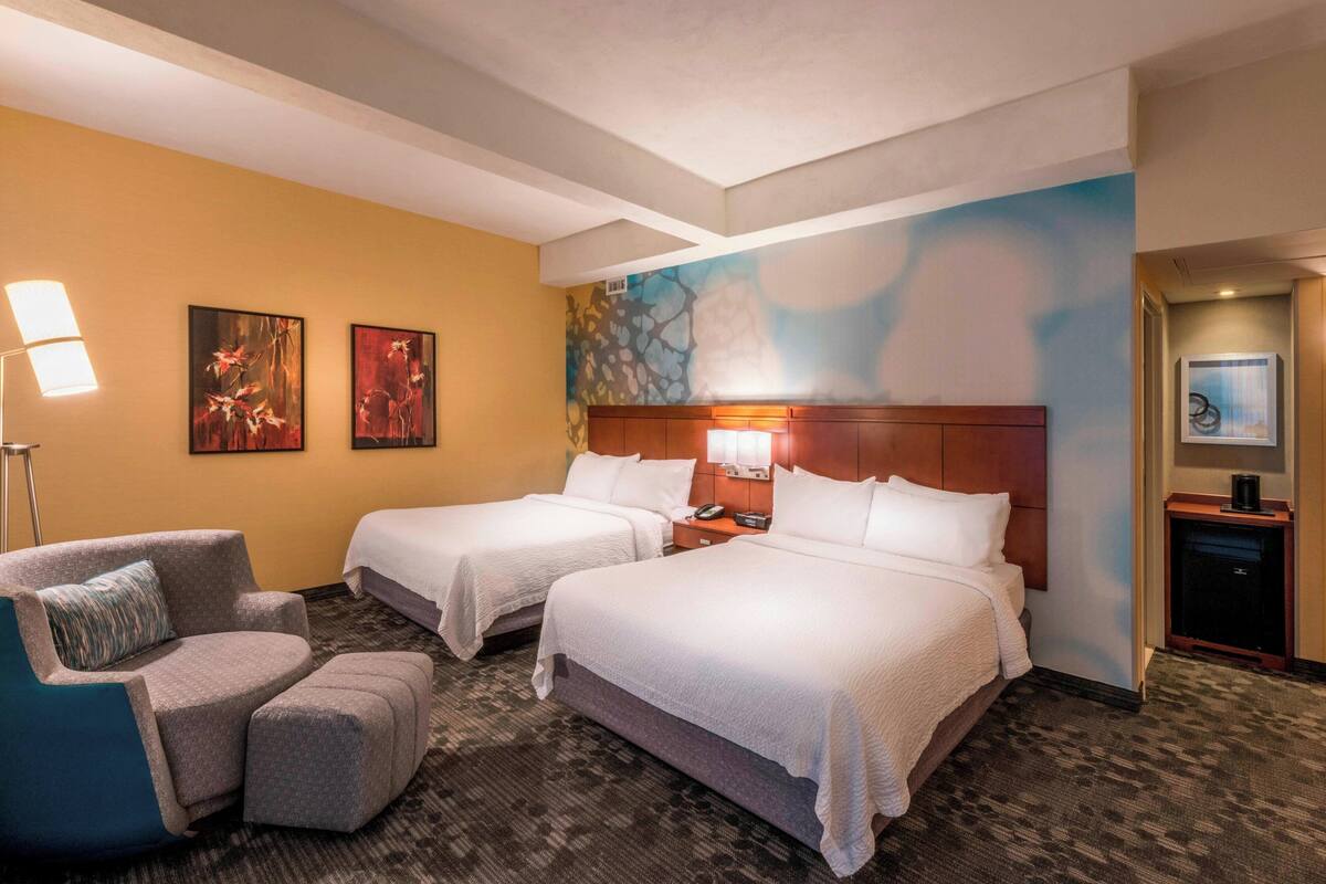A hotel room with two beds, a chair, a nightstand, and artwork on the walls.