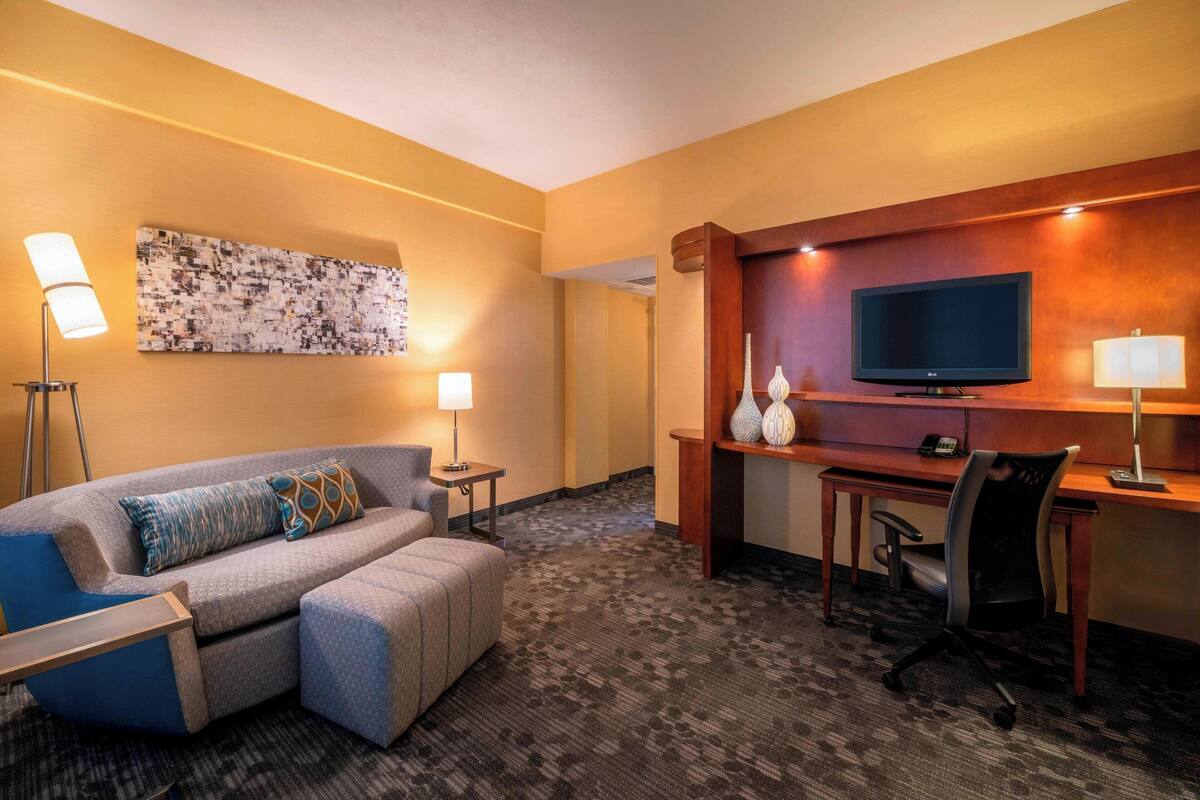 A hotel room with a sofa, a desk, a television, and a lamp.