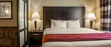 A hotel room with a large bed, two bedside tables with lamps, a chair, and a window with blinds.
