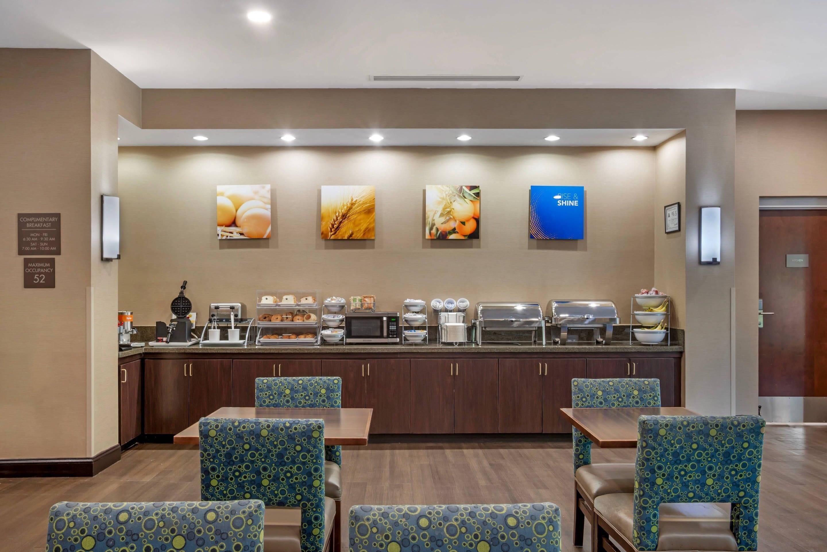 Ein Frühstücksbereich eines Hotels mit Selbstbedienungsbereich, Sitzgelegenheiten und Wandbildern.