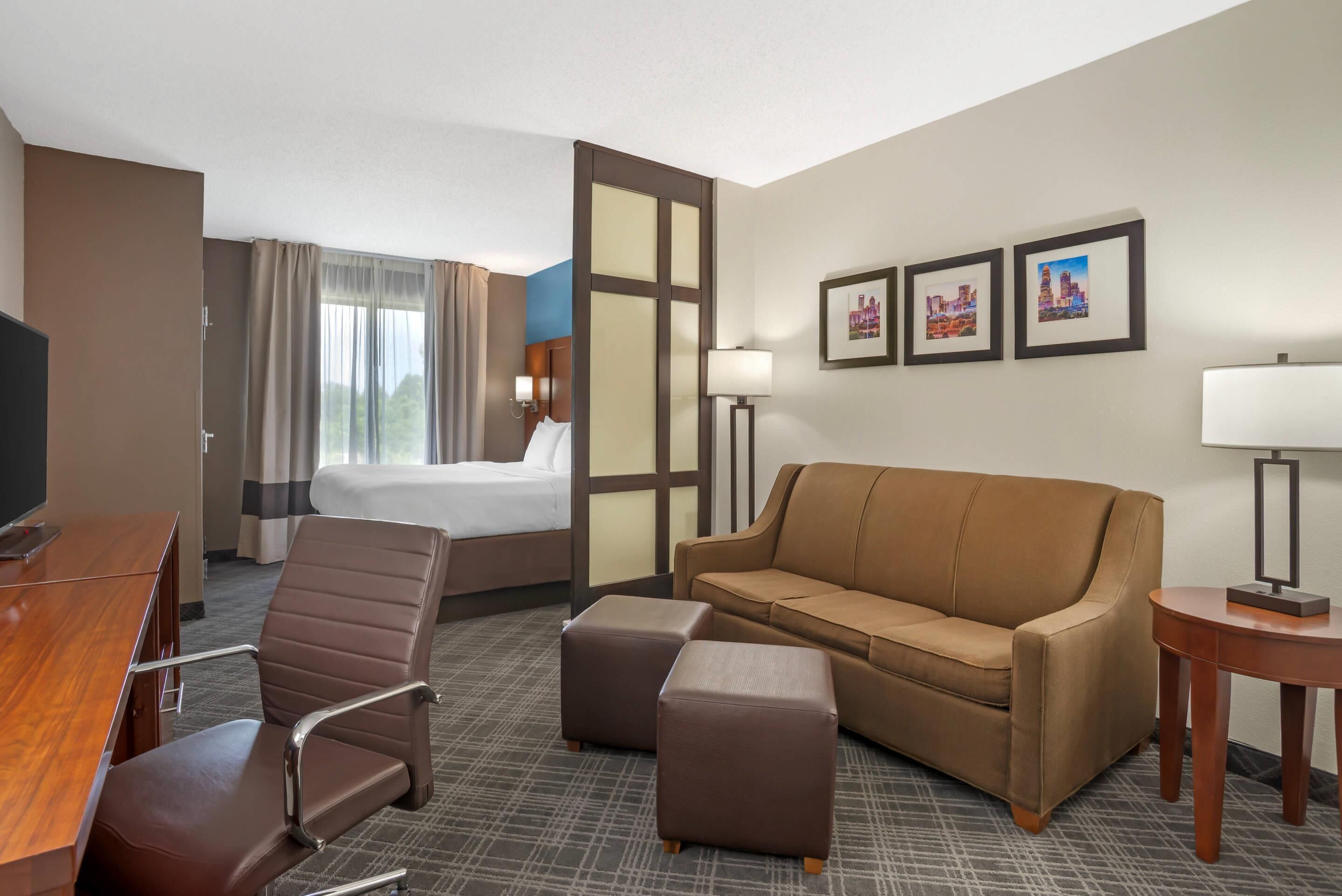 A hotel room with a bed, a sofa, a desk, a chair, a TV, and two framed pictures on the wall.