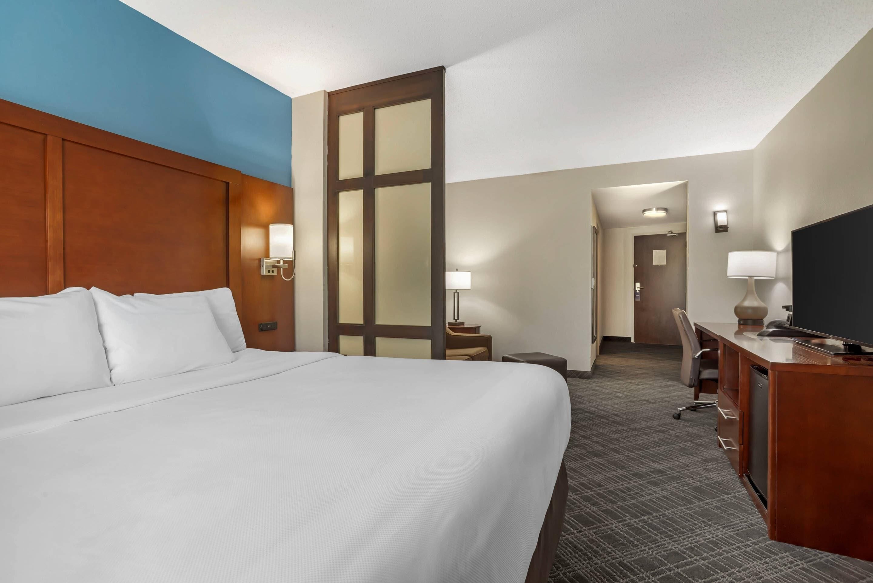 Ein Hotelzimmer mit einem großen Bett, einem Schreibtisch, einem Stuhl und einem Fernseher.