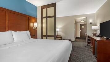 Ein Hotelzimmer mit einem großen Bett, einem Schreibtisch, einem Stuhl und einem Fernseher.