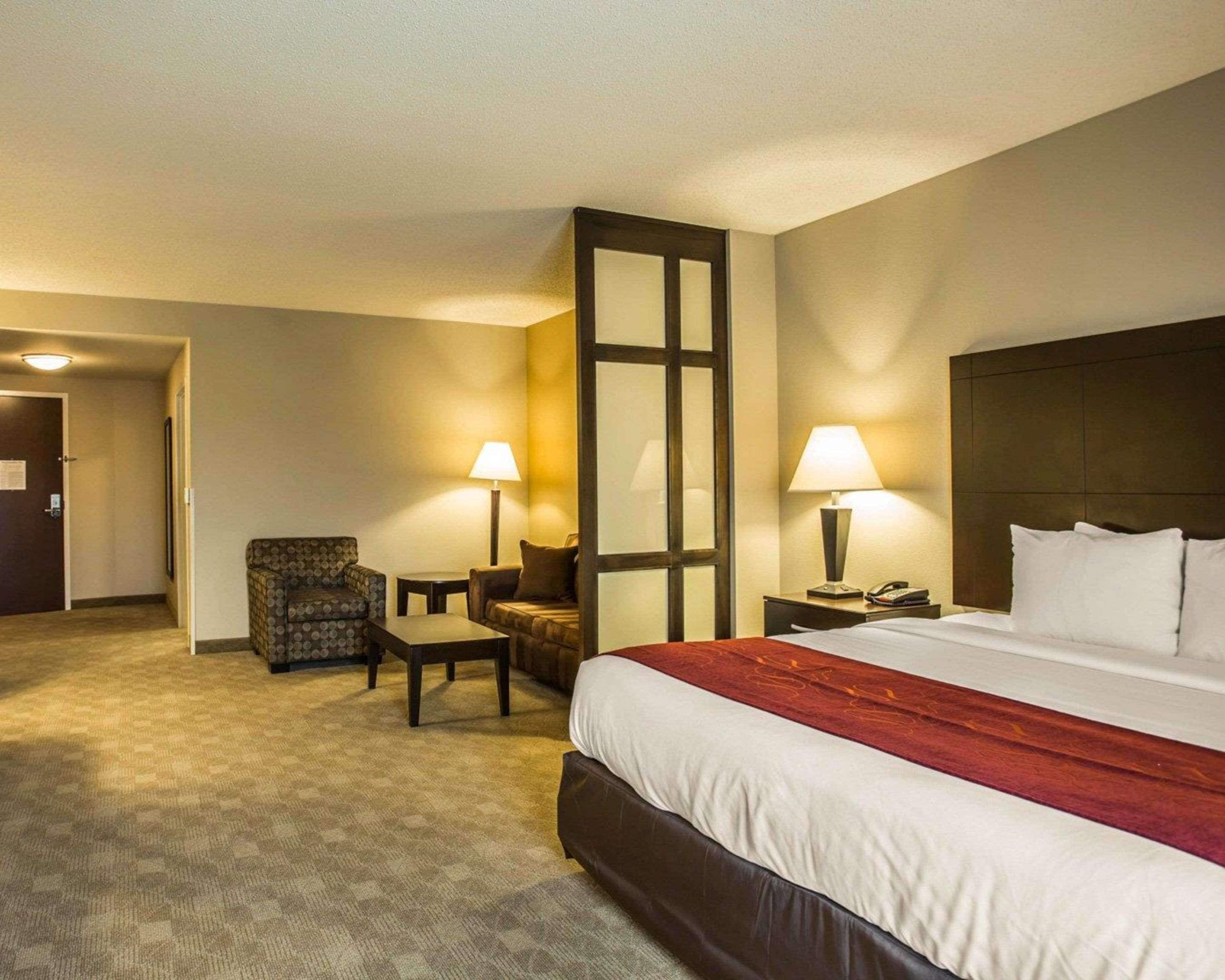 Une chambre d’hôtel avec un grand lit, deux fauteuils, une petite table et deux lampes de chevet.