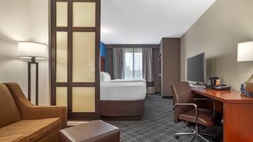 A hotel room with a bed, a desk, a chair, a sofa, and a TV.