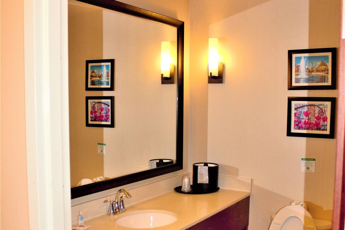 Une salle de bain avec un double lavabo, des toilettes, un grand miroir et deux appliques murales.