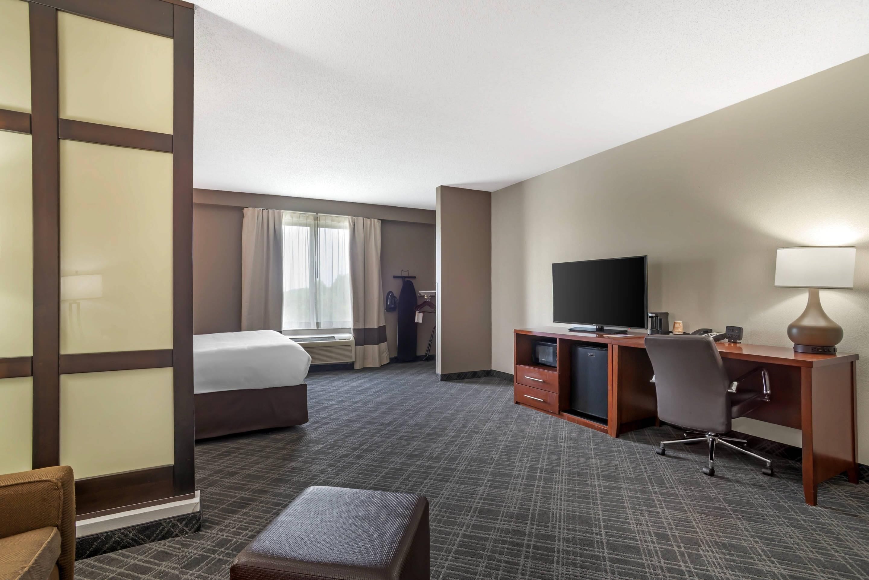 A hotel room with a bed, a desk with a television, a chair, and a small table.