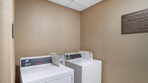 A hotel laundry facility with two Speed Queen commercial dryers, a wall-mounted sign with operating instructions, and a textured beige wall.
