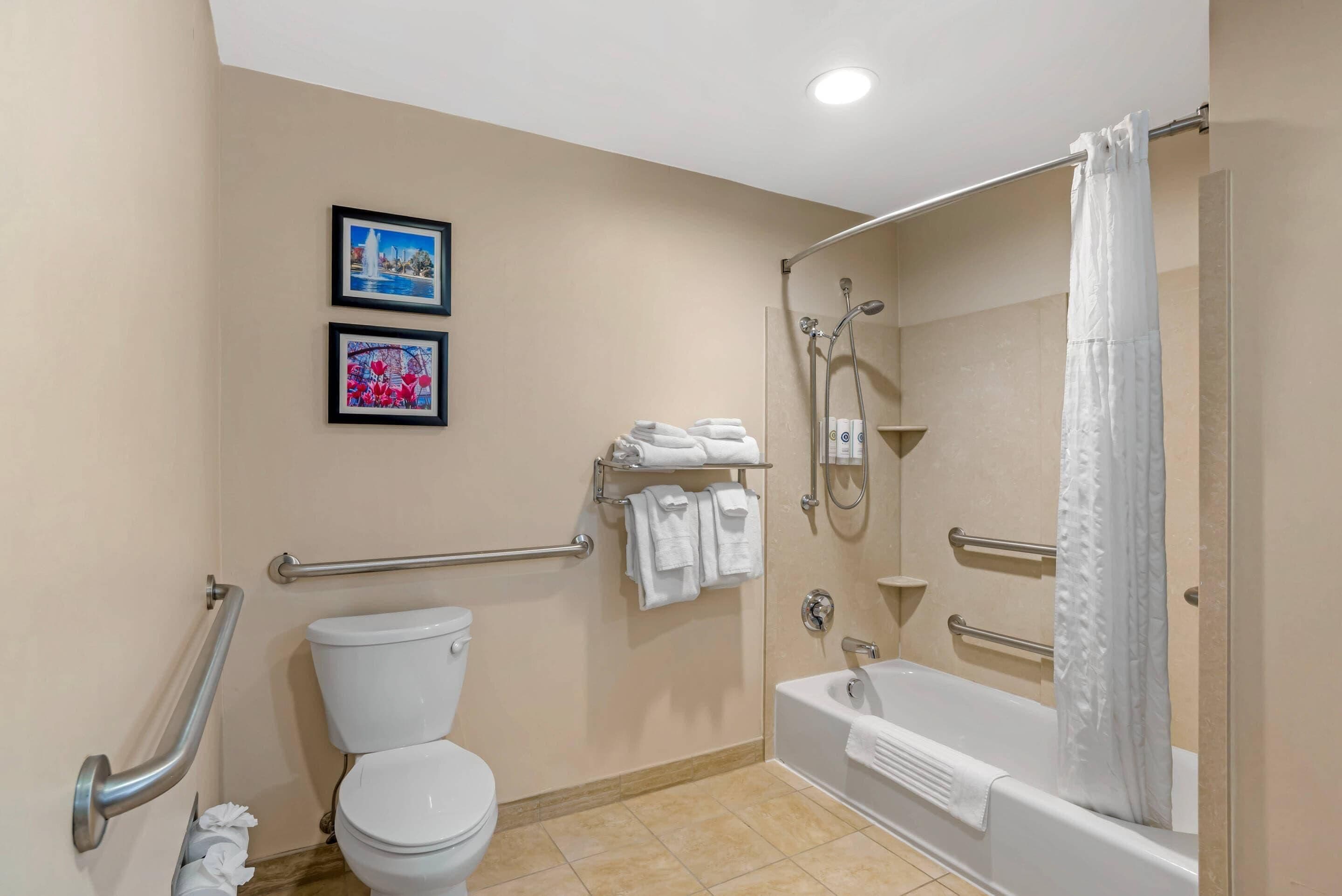 A bathroom with a toilet, a shower, and a bathtub. There are two framed pictures on the wall.