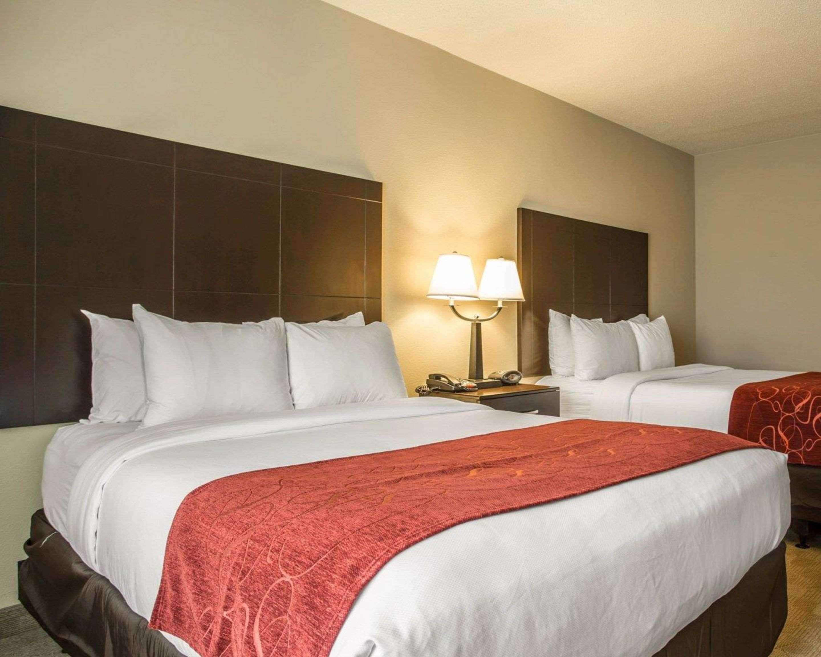 Una habitación de hotel con dos camas, una mesita de noche con una lámpara y un espejo grande en la pared.